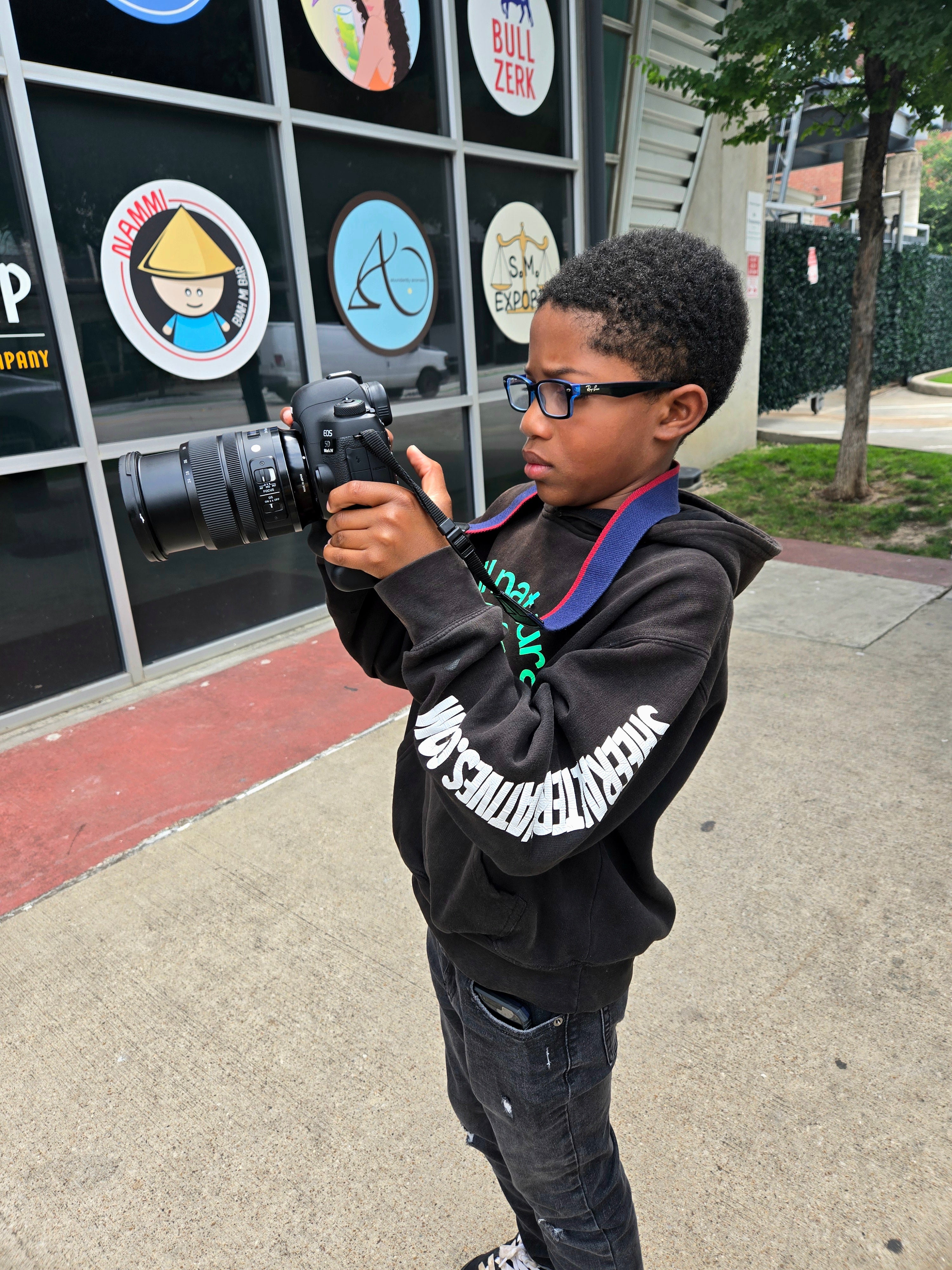 Child holding a camera in front of a store with various signs.