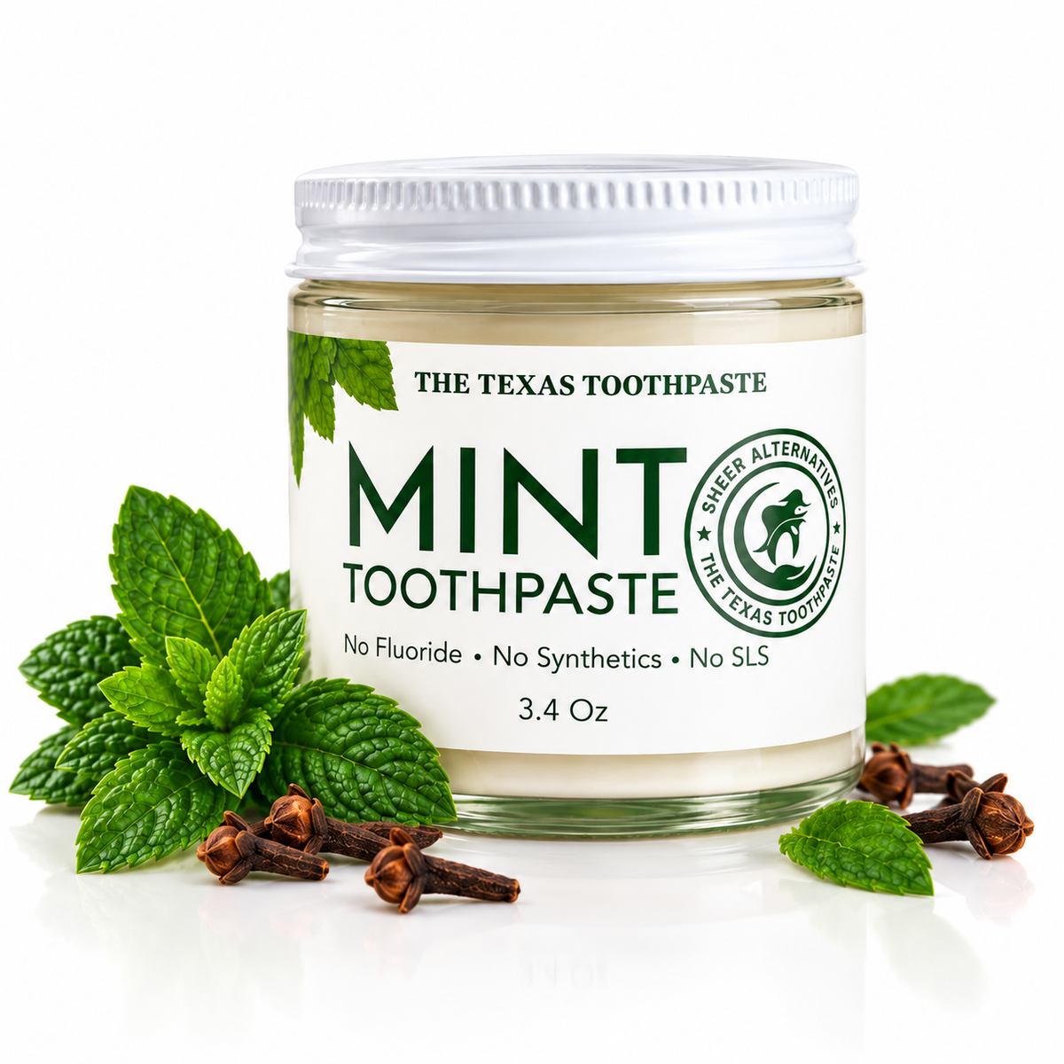 A jar of mint toothpaste with a white lid and white label, surrounded by fresh green mint leaves and whole cloves on a clean white background. The label reads 'THE TEXAS TOOTHPASTE MINT TOOTHPASTE' and shows the brand logo.
